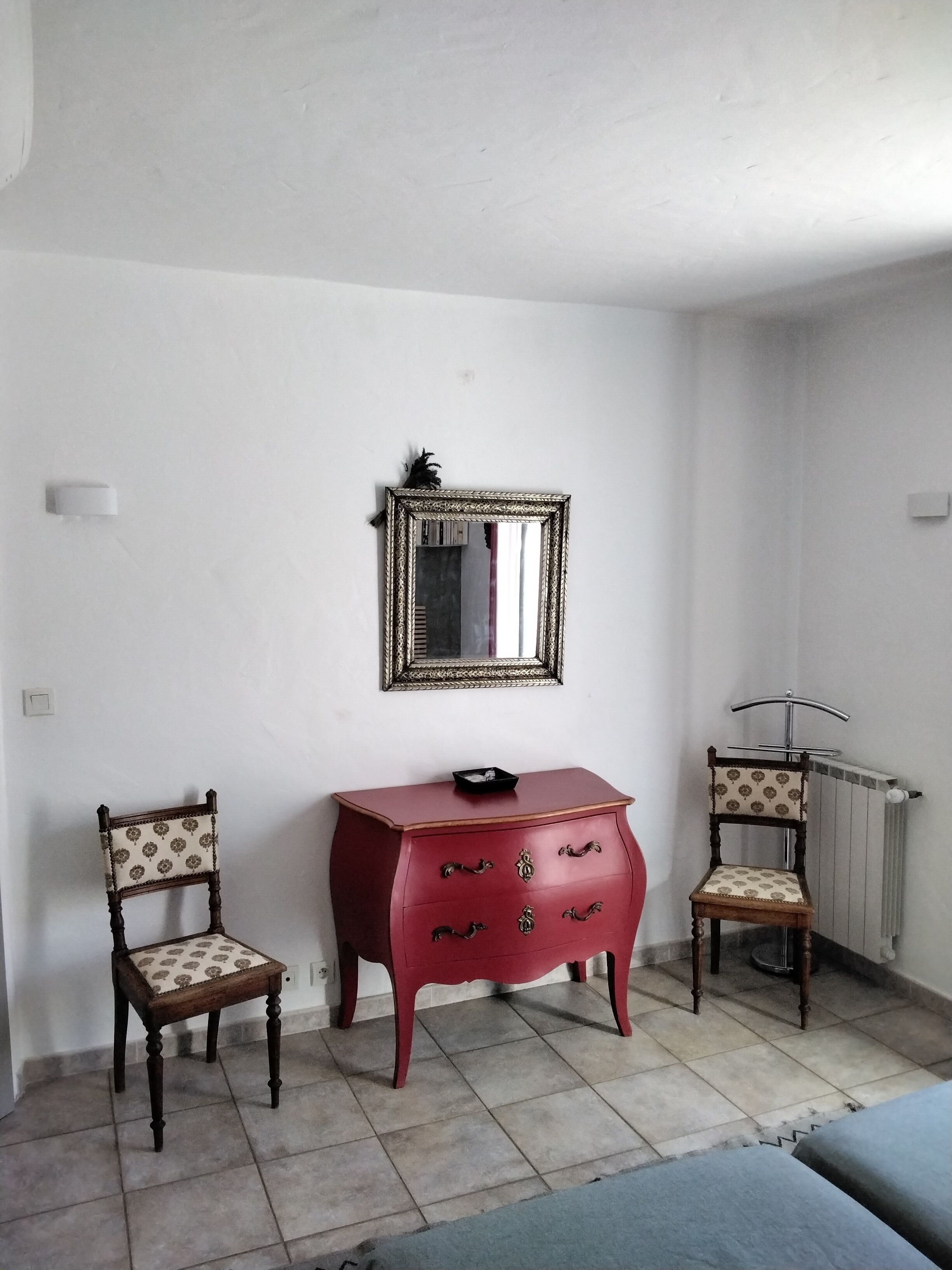 A room with a red dresser, two patterned chairs, a mirror, and a radiator.