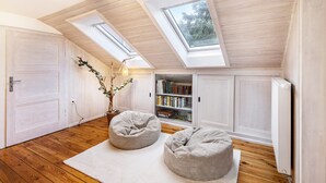 Dormitorio estilo loft con piso de madera, dos sillones orejeros, alfombra blanca, estantería y tragaluces.