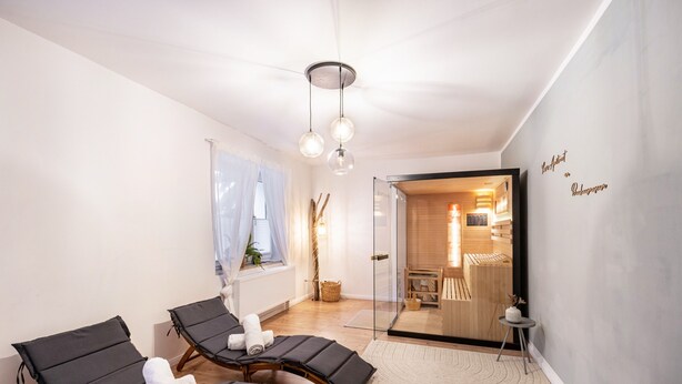 Un cuarto de spa con dos camillas de masaje, una puerta de vidrio que da a una sauna y una pared con un letrero.