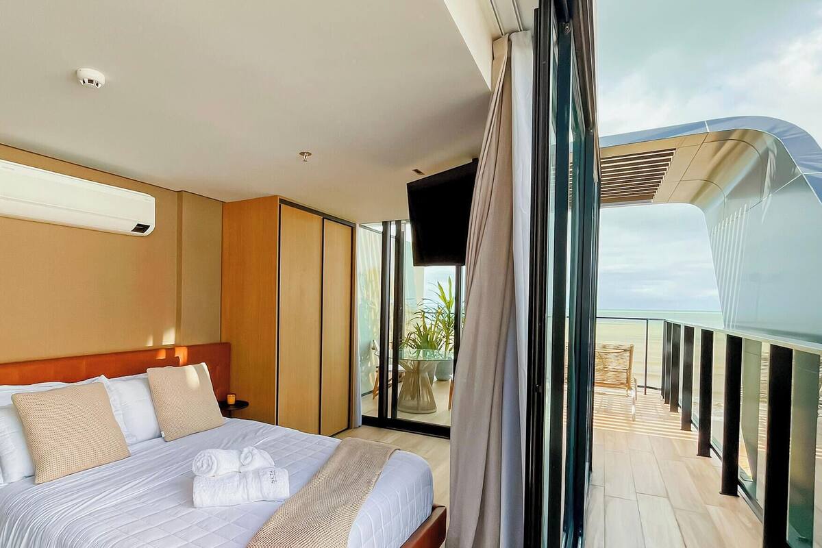 A modern hotel room with a large bed, a bedside table with a lamp, a flat-screen TV, and a balcony with a view.