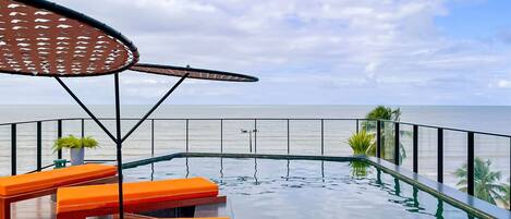 Ein Poolbereich mit orangefarbenen Liegestühlen, einer Pergola und Blick auf das Meer.