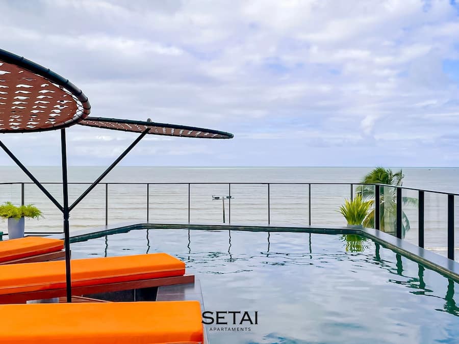 Zona de piscina con sillas reclinables naranja, un pérgola y vista al mar.
