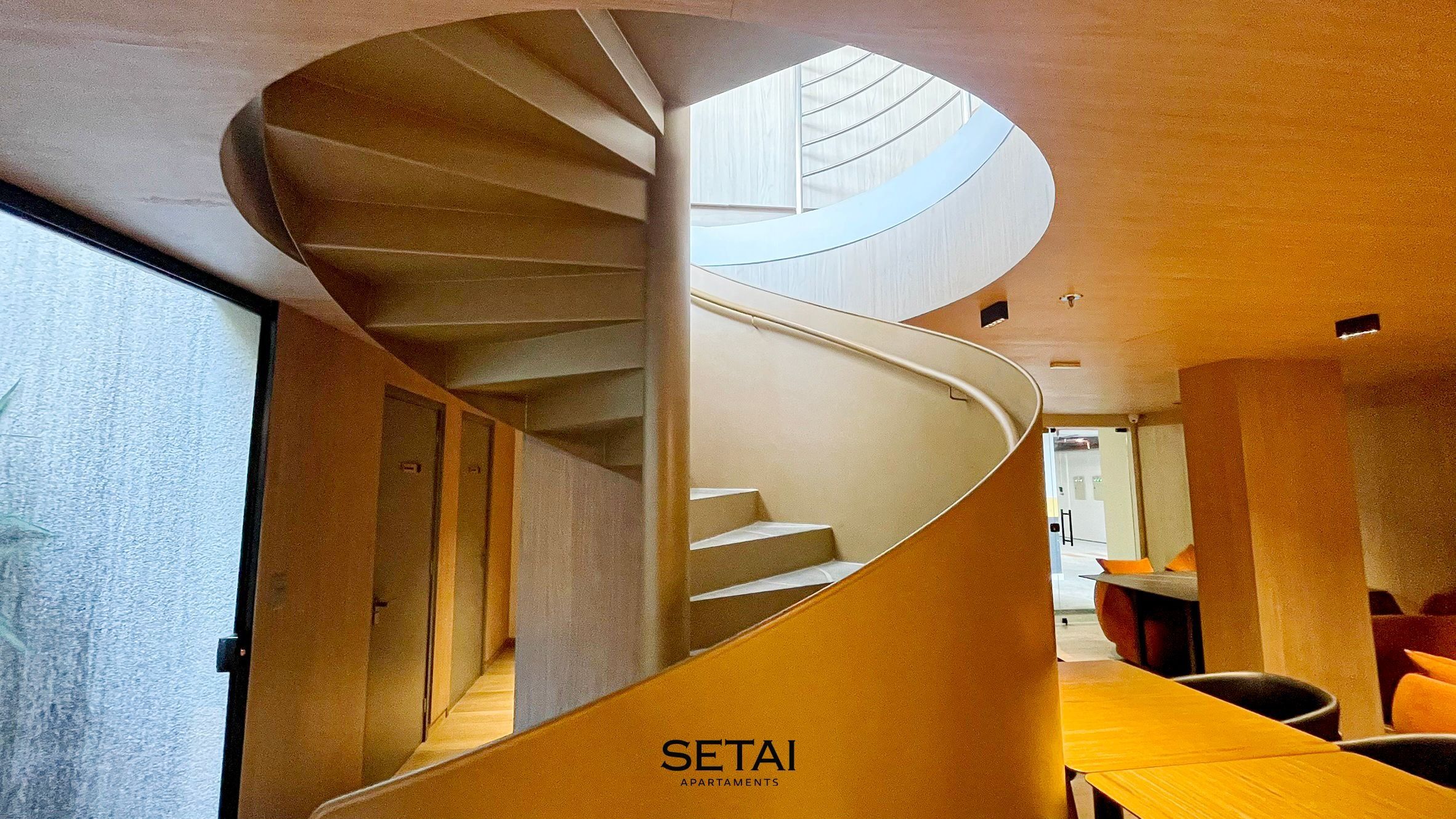 A spiral staircase in a modern interior with a visible office area and a dining space.