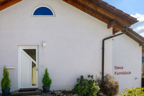 Un bâtiment à l’extérieur blanc, avec un toit en bois, une porte dotée d’un panneau de verre et une enseigne indiquant « Haus Fernblick ».