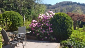 A patio with a table and chairs, surrounded by lush greenery and flowering bushes. - Holiday Home 'Häusle' with Panoramic View, Private Terrace, Covered Balcony & Wi-Fi (Badenweiler)