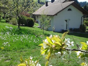 Un bâtiment blanc, surmonté d’un toit en tuiles, entouré d’un champ verdoyant où fleurissent de magnifiques fleurs.