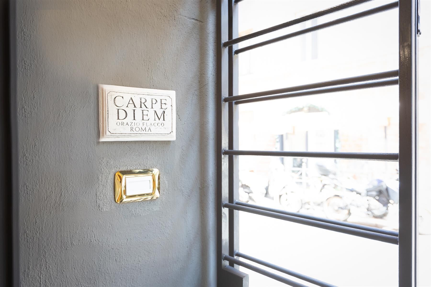 Eine Wand mit einem gerahmten Schild, auf dem ‘CARPE DIEM’ steht, und einem kleinen, goldfarbenen Spiegel.