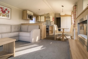 A compact RV interior with a sofa, a dining table, and a kitchenette.