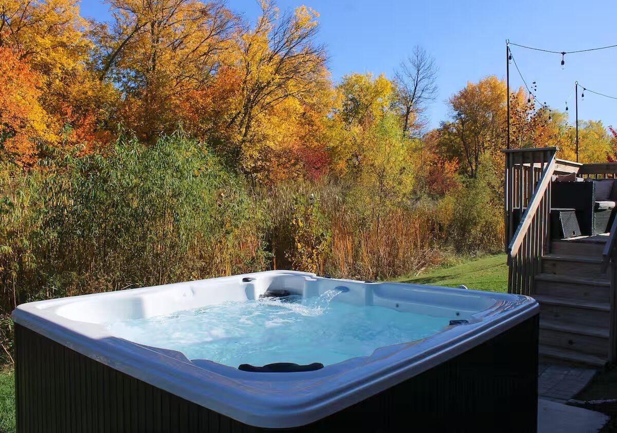 Een hottub in een tuin met herfstkleurige bladeren en houten traptreden.