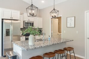 A modern kitchen with white cabinets, stainless steel appliances, a granite countertop, and bar stools.