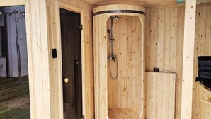 A wooden sauna with a curved design, a shower area, and a small cabinet.