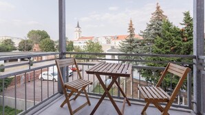 A balcony with two wooden chairs and a table, overlooking a street with a church tower and trees. - Apartment 'Wellness Lounge Am Bauhausmuseum' with Balcony and Wi-Fi (Dessau)