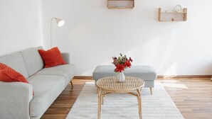 A modern living room with a grey sofa, a round wicker coffee table, and a small grey ottoman. - Apartment 'Wellness Lounge Am Bauhausmuseum' with Balcony and Wi-Fi (Dessau)