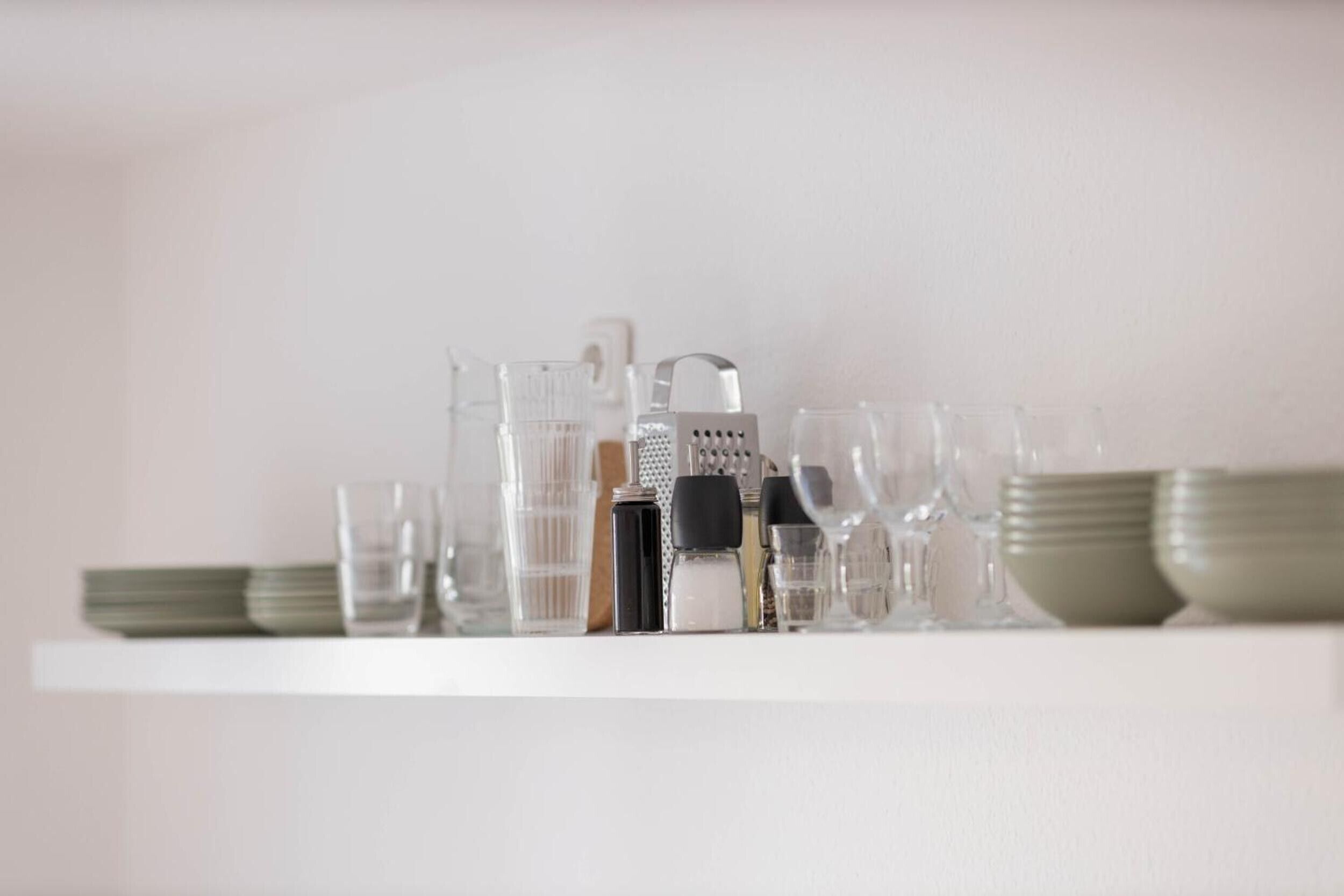 Une étagère blanche sur laquelle sont disposés divers objets en verre et ustensiles de cuisine.