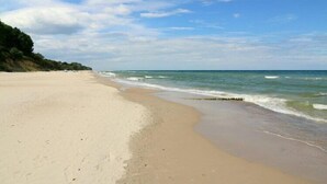Ein weiter Sandstrand mit sanften Wellen, einem klaren Himmel und einer fernen Küstenlinie mit Vegetation.