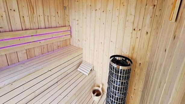Eine Holzsauna mit einer Bank, einem Metallofen und einem Holzwaschbecken.