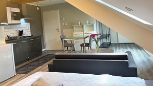 Ett kompakt kök med moderna vitvaror, en matplats med ett glasbord och stolar samt en mysig sittgrupp med en soffa och ett litet bord.