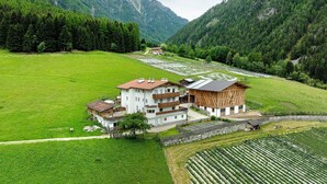 A multi-story building with a balcony, surrounded by a lush green field and mountains in the background.