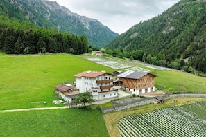 A multi-story building with a balcony, surrounded by a lush green field and mountains in the background.