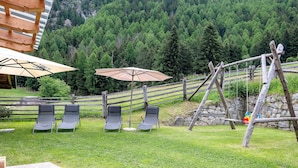 A patio with lounge chairs and umbrellas, a wooden swing set, and a stone wall.