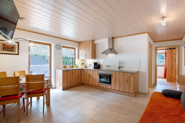 A modern kitchen with wooden cabinets, a built-in oven, and a dining area with wooden chairs and a table.