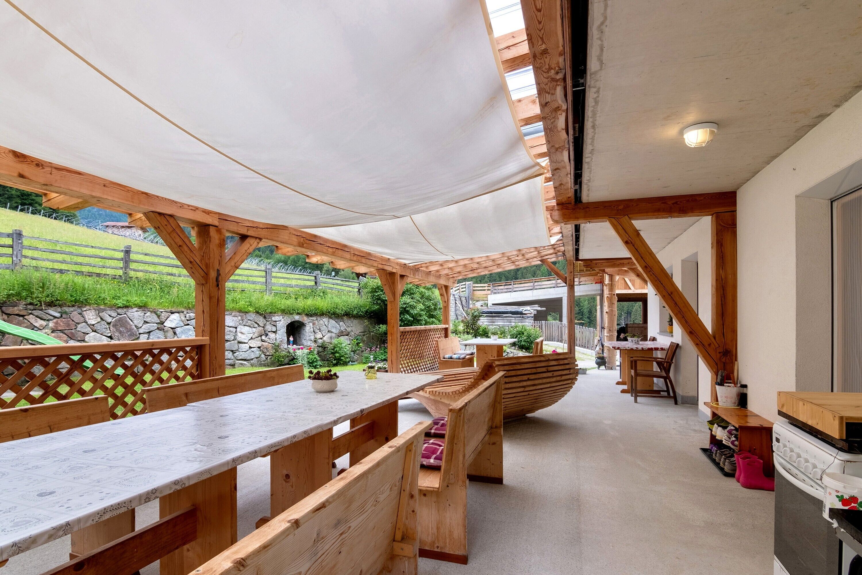 Un'area patio all'aperto con panche e tavoli in legno, un muro in pietra e vista su un paesaggio verdeggiante.