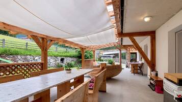 Un'area patio all'aperto con panche e tavoli in legno, un muro in pietra e vista su un paesaggio verdeggiante.
