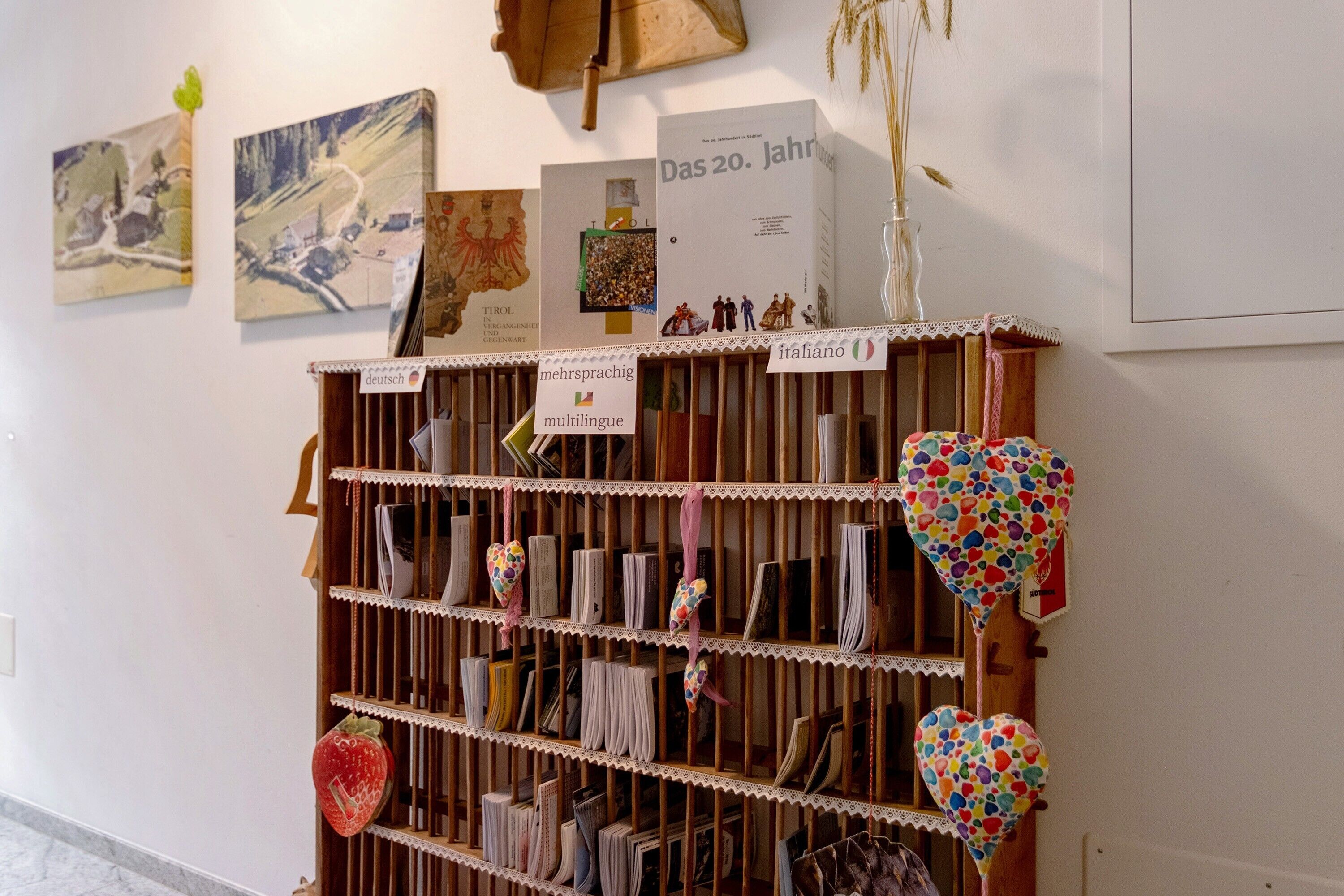 Ein Bücherregal mit Büchern und Dekoration, eine Wand mit gerahmten Bildern und ein Schild, das sprachliche Bereiche ausweist.