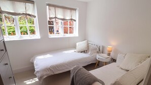 Un dormitorio con dos camas individuales, una mesita de noche con lámpara, un armario y una ventana con vistas a zonas verdes.