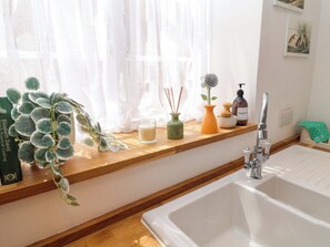 A kitchen with a wooden countertop, a white sink, a window with sheer curtains, and a potted plant. - 11 Ballygate (Beccles)
