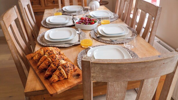 Una mesa de madera dispuesta con platos, vasos, un cuenco de fruta y cruasanes.