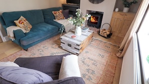 Una sala de estar acogedora con un sofá azul verdoso, una mesa de centro con un florero, una chimenea y un espejo grande en la pared.