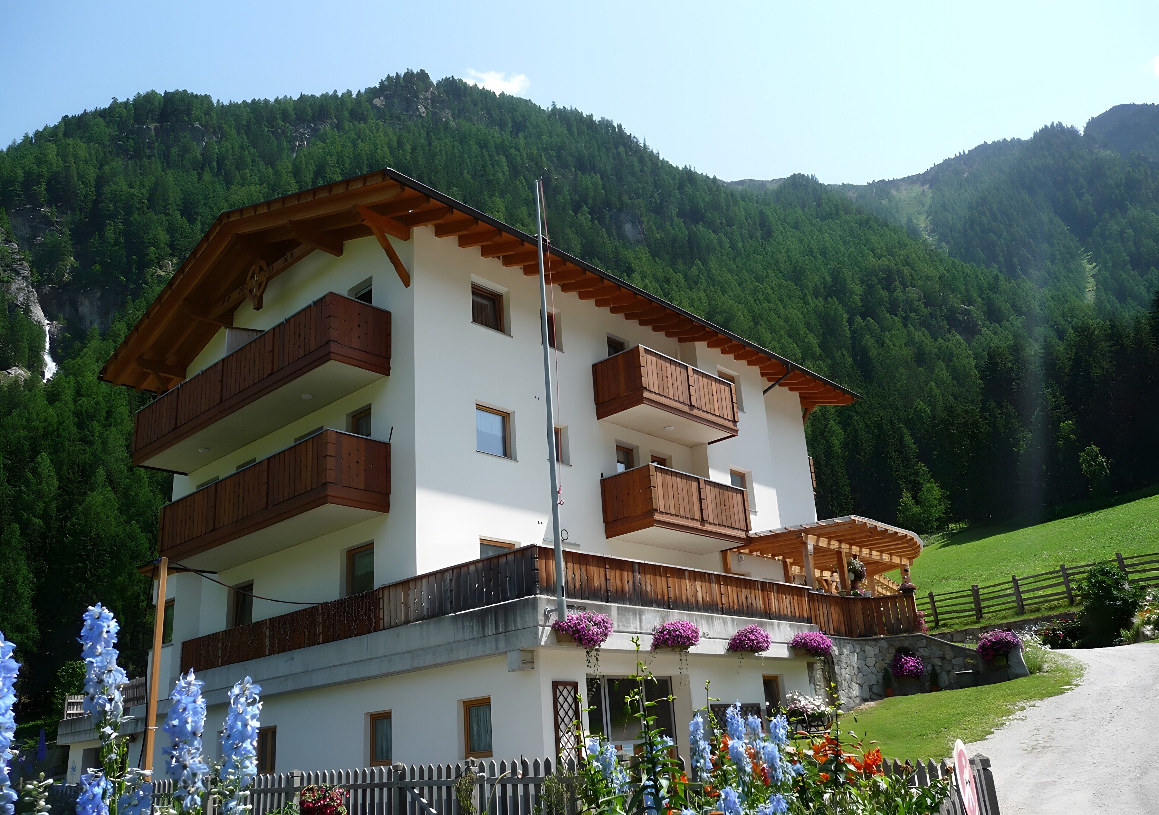 Ein mehrgeschossiges Gebäude mit Balkonen, einer Holzfassade und einem Bergpanorama im Hintergrund.