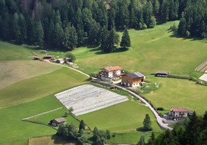 Vue aérienne d’une propriété rurale comprenant plusieurs bâtiments, notamment une maison principale avec un toit rouge, une grange et une installation de panneaux solaires.