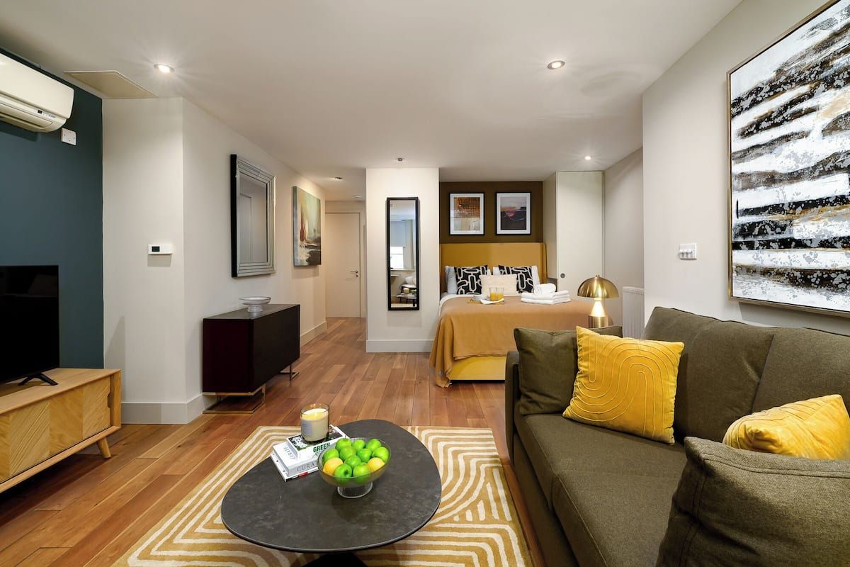 Een moderne hotelkamer met een bed, een bank, een televisie en een zithoek met een tafel en stoelen.