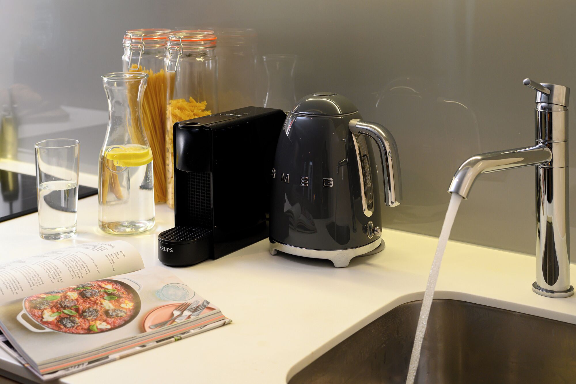 A kitchen counter with a coffee maker, a kettle, a glass of water, and a cookbook.