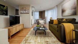 Ein modernes Wohnzimmer mit einer Couch, einem Couchtisch und einem Fernseher. Im Hintergrund befindet sich ein Essbereich mit Tisch und Stühlen.