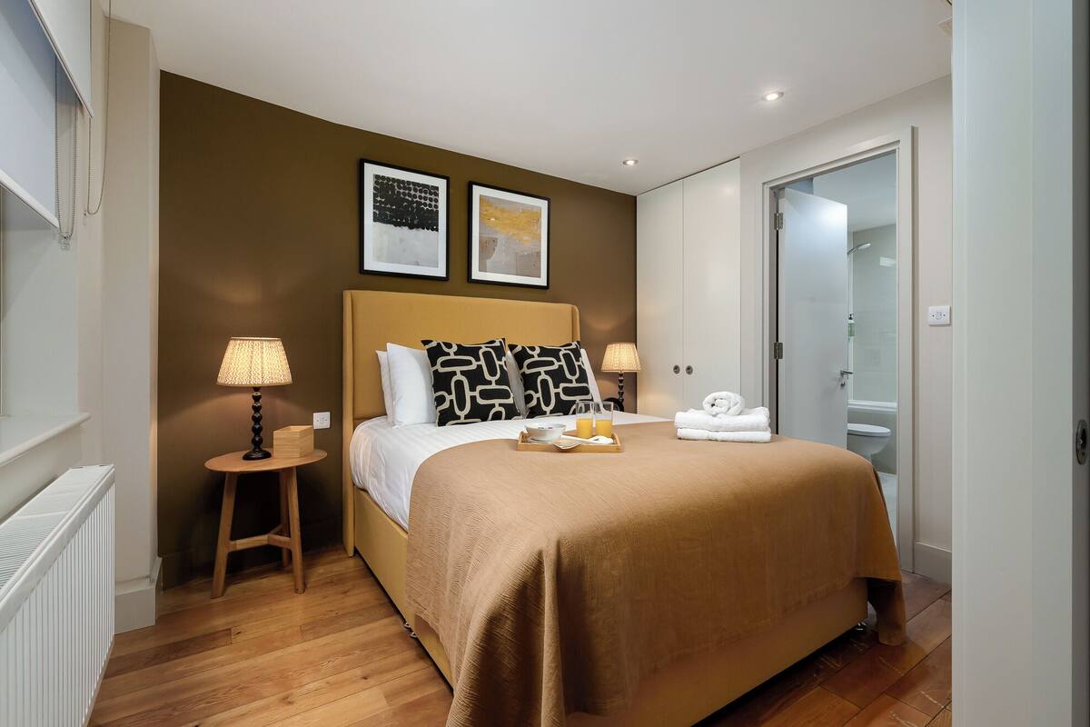 Een hotelkamer met een bed, nachtlampjes, een dienblad met ontbijtartikelen en een badkamer zichtbaar door een geopende deur.