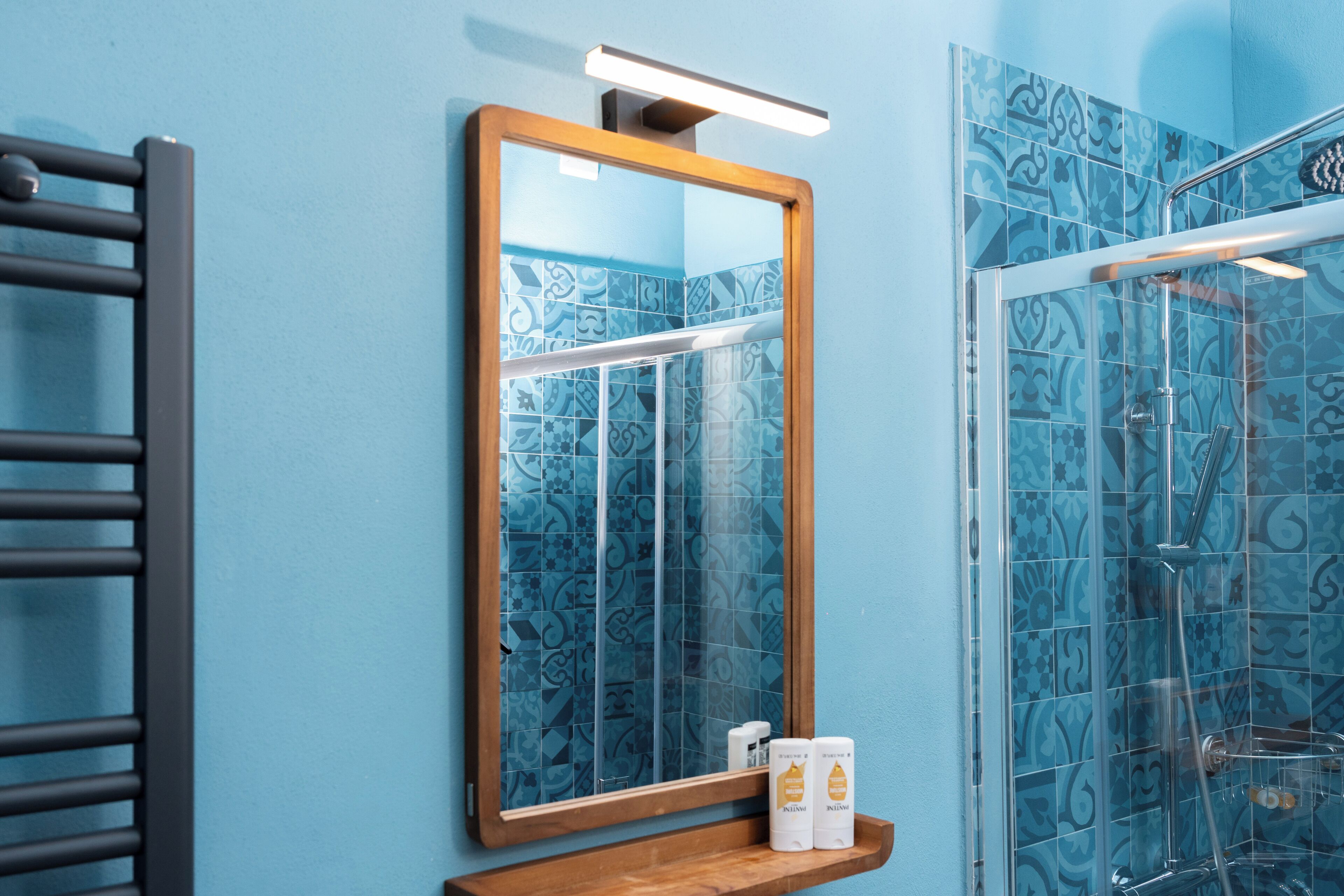 Un bagno con una parete rivestita in piastrelle blu, uno specchio con cornice in legno e uno spazio doccia in vetro.
