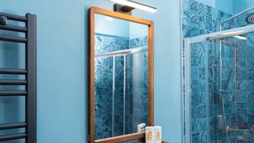 Un bagno con una parete rivestita in piastrelle blu, uno specchio con cornice in legno e uno spazio doccia in vetro.