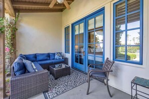 Ein überdachter Patio-Bereich mit einer blauen Rutschtür, einem Korbsessel, einem Sessel und einem kleinen Tisch.