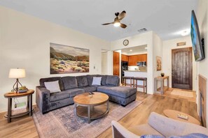 A living room with a sectional sofa, a coffee table, and a painting on the wall. - Heritage Hideaway A | 1BR Legacy Villa (La Quinta)
