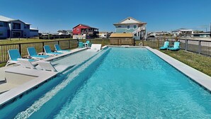 A rectangular swimming pool with clear blue water, surrounded by a wooden deck and multiple lounge chairs. - Inn at Dolphin Bay | Downtown, Garden View (Rockport)