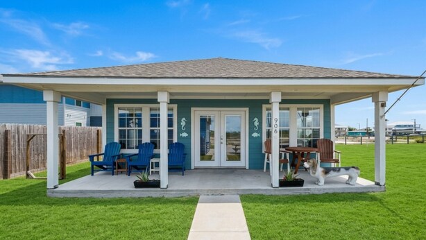 A house with a covered porch, blue chairs, a table, and a dog. - Inn at Dolphin Bay | Downtown, Garden View (Rockport)