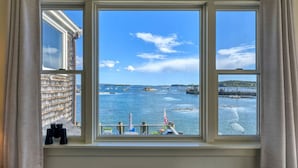 A room with a large window overlooking a harbor with boats and a clear sky. - Inn on the Harbor (Stonington)
