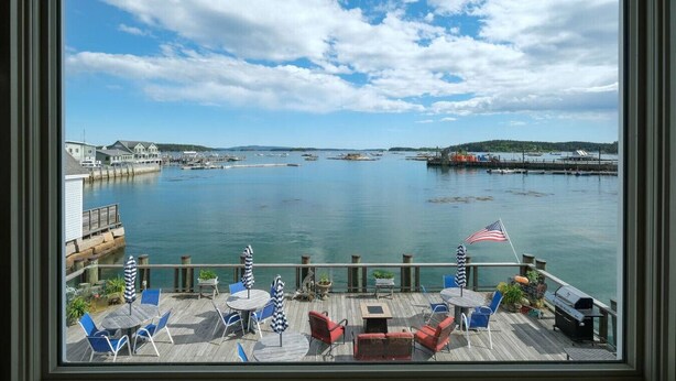 A waterfront patio with outdoor seating, a view of the harbor, and a clear sky. - Inn on the Harbor (Stonington)