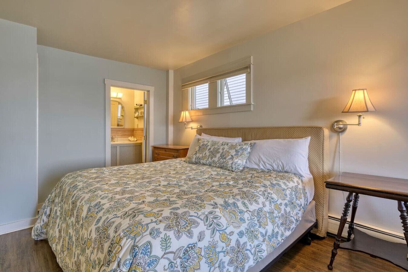 Un dormitorio con cama, lámparas de noche, mesita de noche y ventana con persianas.