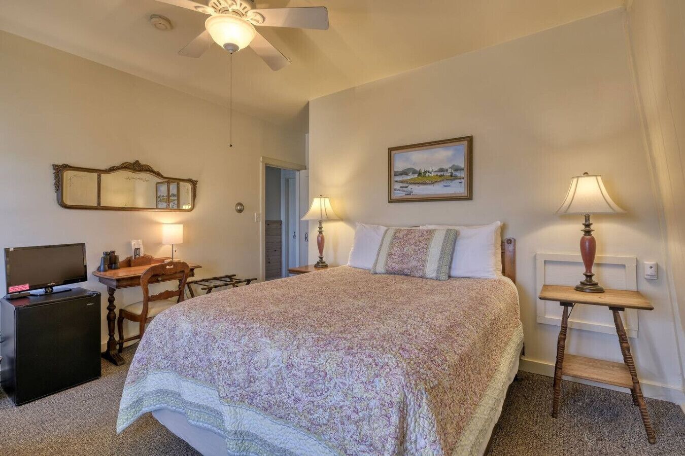Une chambre à coucher comprenant un lit, un bureau, une chaise, un téléviseur et un ventilateur de plafond.