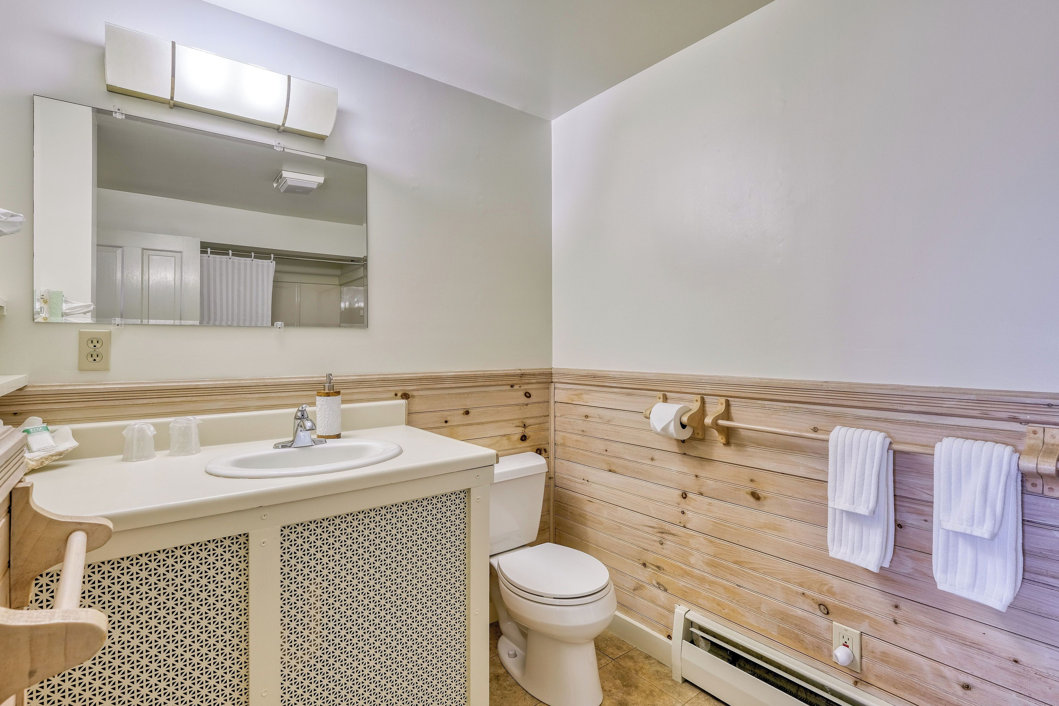 A bathroom with a wooden panel wall, a sink with a mirror above it, a toilet, and two towels hanging on a rack.