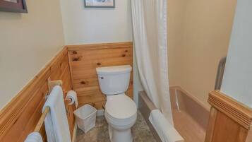 Un baño con tocador de madera, inodoro, bañera y cortina de ducha.